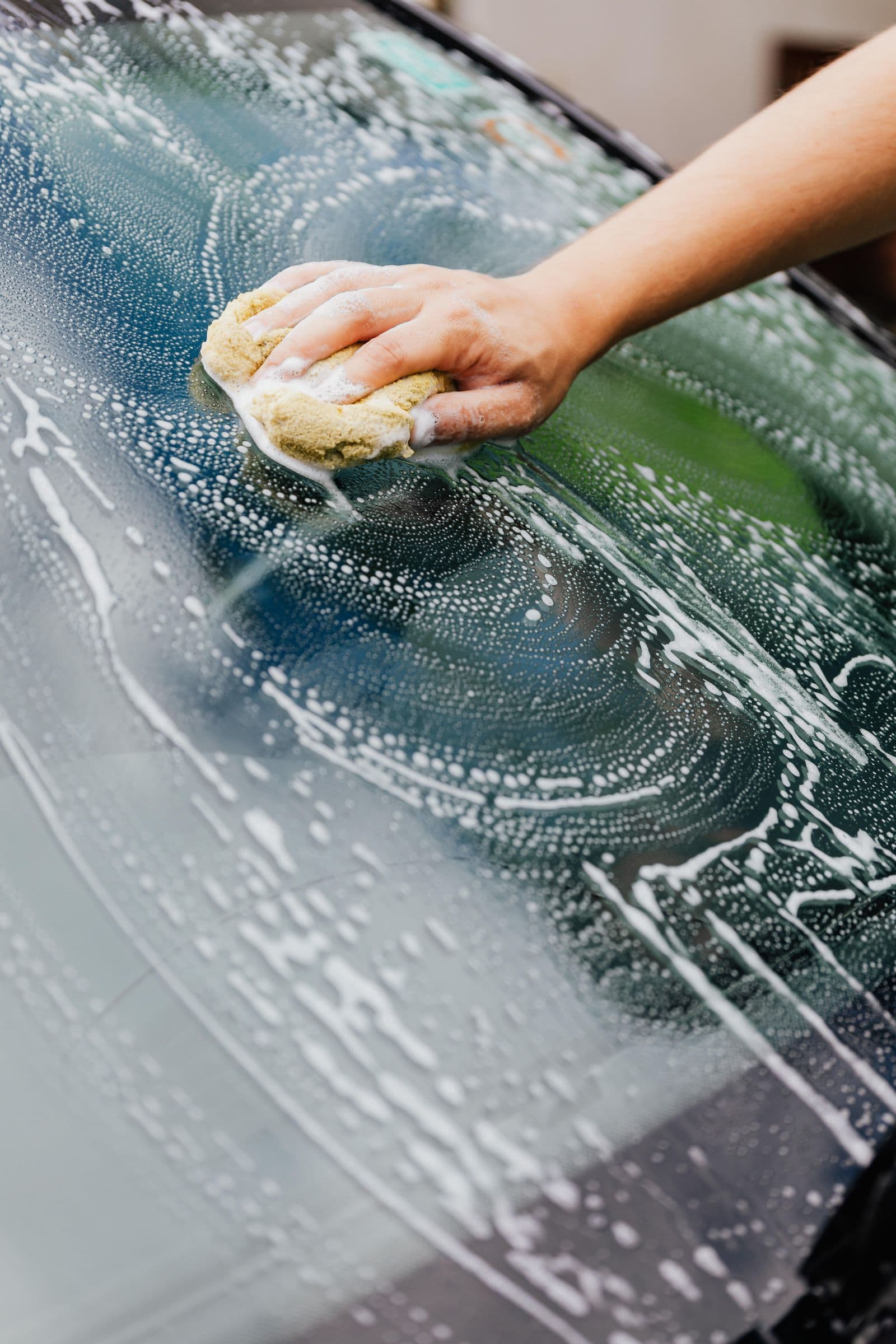 Hand cleaning a windscreen edge where wiper grime collects